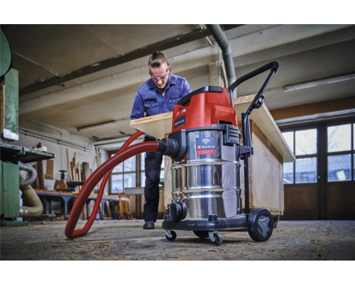 Scène d'atelier avec un aspirateur eau et poussière Einhell et un homme travaillant une planche de bois