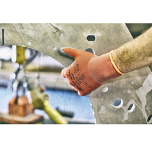 Eine Hand mit Arbeitshandschuh berührt ein Metallstück mit Löchern.