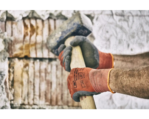 Mann mit Handschuhen bearbeitet Mauerwerk mit einem Fäustel