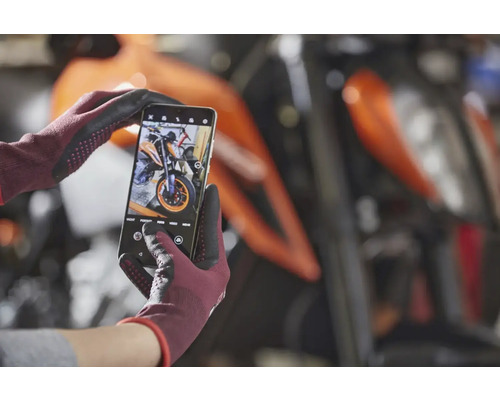 Un smartphone dans des mains gantées photographie une moto.
