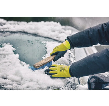 Une personne portant des gants d'hiver nettoie un pare-brise enneigé avec une brosse.