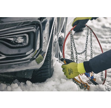 Une personne monte des chaînes à neige sur un pneu de voiture en hiver