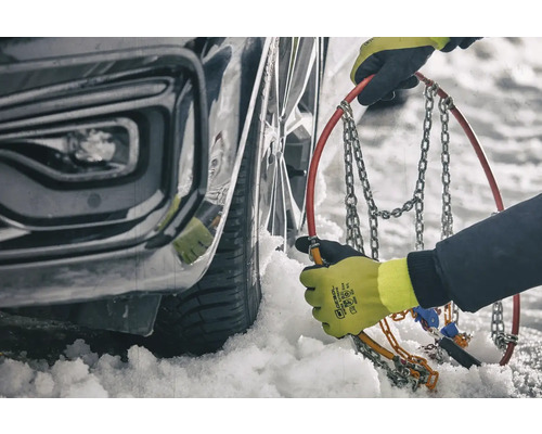 Une personne monte des chaînes à neige sur un pneu de voiture en hiver