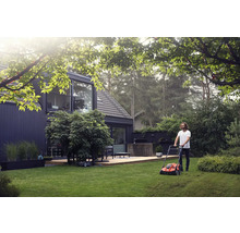 Mann mäht Rasen mit einem Rasenmäher in einem Garten vor einem modernen Haus.