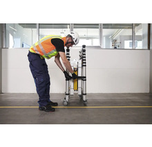 Une personne sécurise un échafaudage roulant plié avec une sangle.