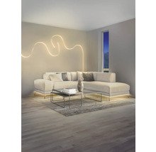 Salon moderne avec canapé en L, applique murale LED décorative en forme de vague et éclairage LED indirect sous le canapé.