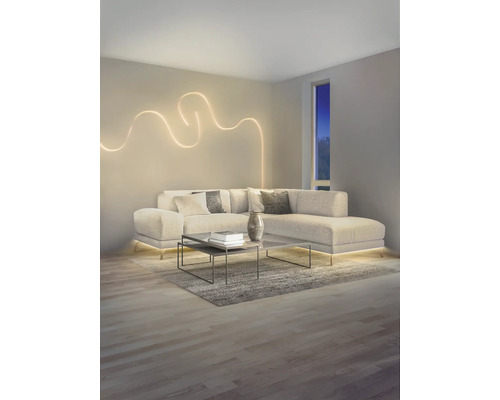 Salon moderne avec canapé en L, applique murale LED décorative en forme de vague et éclairage LED indirect sous le canapé.