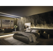 Chambre à coucher moderne avec salle de bains intégrée, mur d accent aspect pierre, baignoire îlot noire et lit rembourré sur parquet.