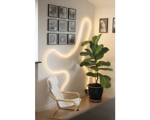 Pièce lumineuse avec un ruban LED flexible au mur, un fauteuil et une grande plante d'intérieur en pot.