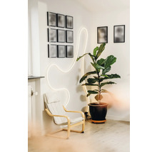 Salon moderne avec un fauteuil blanc, une grande plante verte en pot et un ruban lumineux LED ondulé sur un mur blanc.