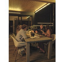 Quatre personnes assises à une table en bois sur une terrasse en bois la nuit, éclairée par des bandes LED au plafond et sur les murs.