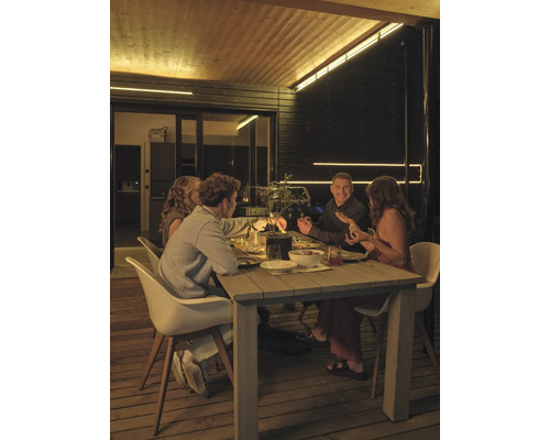 Quatre personnes assises à une table en bois sur une terrasse en bois la nuit, éclairée par des bandes LED au plafond et sur les murs.