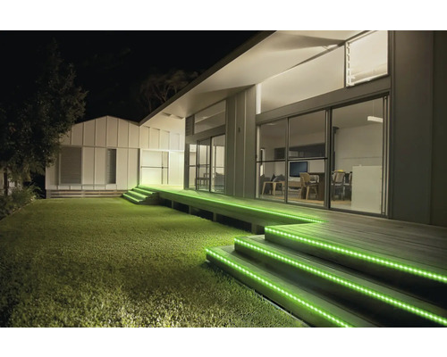 Éclairage extérieur d une terrasse moderne de nuit avec des rubans LED verts sur les marches en bois.