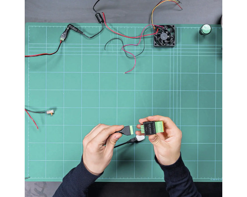Mains connectant un câble à un module SSR ADDON sur un plan de travail avec des composants électroniques tels qu'un ventilateur et des câbles.