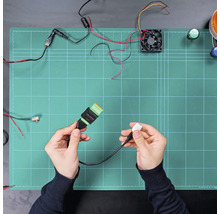 Câble de raccordement électronique avec connecteur USB et bornier, tenu dans les mains au-dessus d'un tapis de travail avec composants.