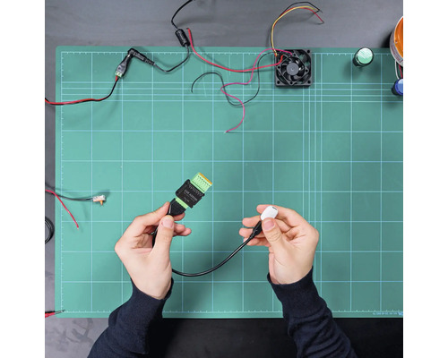 Câble de raccordement électronique avec connecteur USB et bornier, tenu dans les mains au-dessus d'un tapis de travail avec composants.