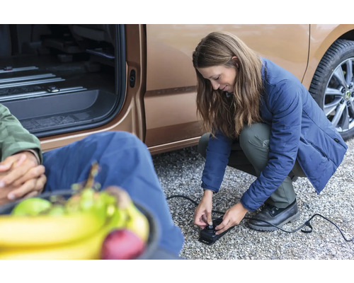 Frau bedient eine elektrische Luftpumpe neben einem Fahrzeug