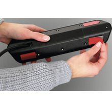 Une personne fixe un bloc multiprise avec des bandes adhésives.