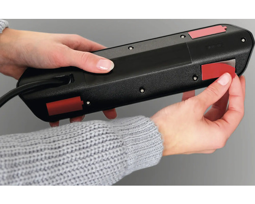 Une personne fixe un bloc multiprise avec des bandes adhésives.