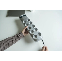 Une personne tient un bloc multiprise gris avec dix prises.