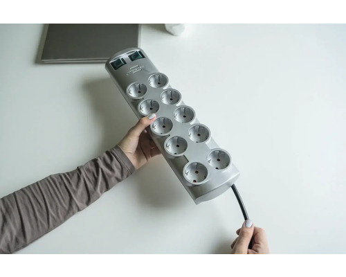 Une personne tient un bloc multiprise gris avec dix prises.