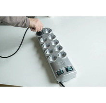 Une personne branche une fiche dans une multiprise grise à dix prises