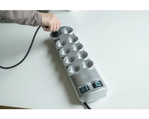 Une personne branche une fiche dans une multiprise grise à dix prises