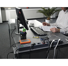 Arbeitsplatz mit Steckerleiste, elektronischen Geräten und Person