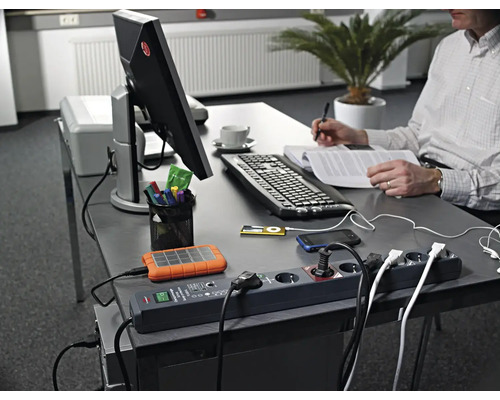 Arbeitsplatz mit Steckerleiste, elektronischen Geräten und Person