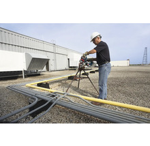 Un homme en vêtements de travail coupe des tuyaux sur un toit avec une scie à tubes.