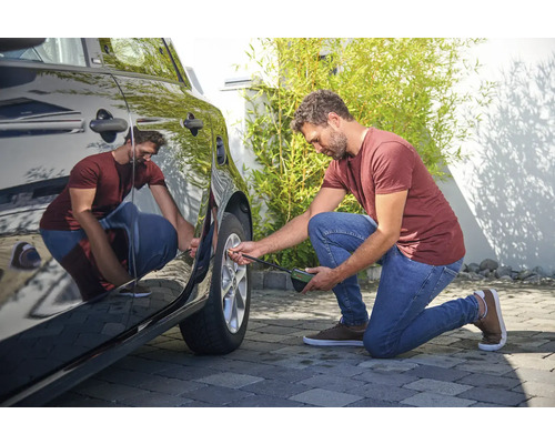 Un homme vérifie la pression d'un pneu de voiture avec un manomètre.