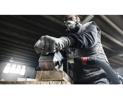 Un homme ponce un morceau de bois avec une ponceuse. Il porte un masque de protection et des lunettes de protection.