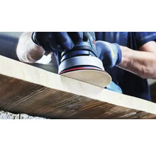 Eine Person schleift ein Holzbrett mit einem Exzenterschleifer.