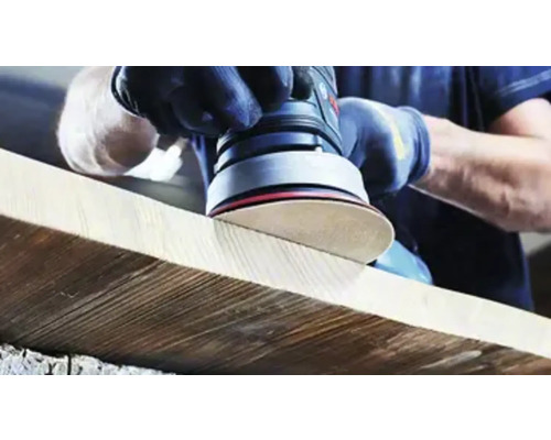 Eine Person schleift ein Holzbrett mit einem Exzenterschleifer.