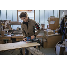 Une personne ponce une planche de bois avec une ponceuse excentrique dans un atelier.