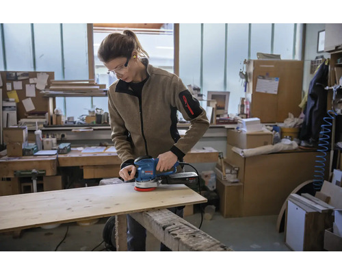 Une personne ponce une planche de bois avec une ponceuse excentrique dans un atelier.