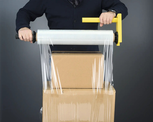 Mann verpackt Kartons mit einer Hand Stretchfolie mit Griff.