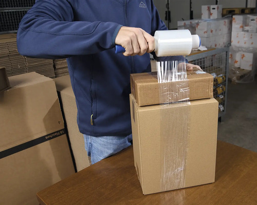 Mann verpackt Kartons mit Stretchfolie