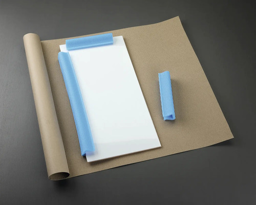 Verpackungsmaterialien: Glasplatte, Papierrolle, Wellpappe und Schaumstoffschutz.