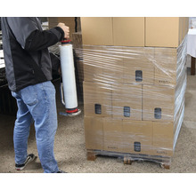 Eine Person verpackt Kartons mit einem Folienwickler auf einer Palette.