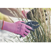 Une personne coupe de l'herbe avec un sécateur et porte des gants de jardinage.