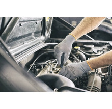 Un mécanicien travaillant sur un moteur de voiture avec des gants de protection.