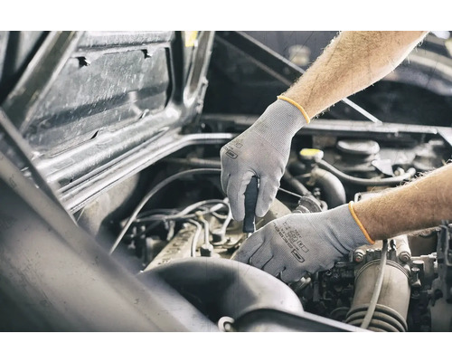 Un mécanicien travaillant sur un moteur de voiture avec des gants de protection.