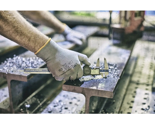 Une personne mesure une pièce métallique avec un pied à coulisse numérique sur un support.