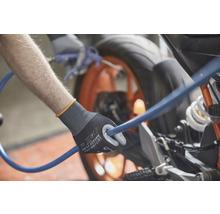 Eine Person hält einen blauen Schlauch mit einem Paar Arbeitshandschuhen in der Hand und reinigt ein Motorrad.