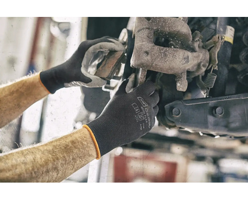 Mechanikerhände arbeiten an einem Autorad mit Schutzhandschuhen.