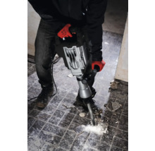 Ein Mann mit Arbeitshandschuhen benutzt einen Abbruchhammer, um Fliesen zu entfernen.