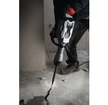 Ein Mann benutzt einen Abbruchhammer, um einen Riss in einen Betonboden zu schlagen.