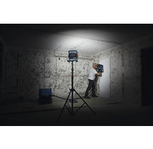 Ein Mann arbeitet mit einer Mauernutfräse in einem Raum, der von einem Baustrahler beleuchtet wird. Ein Staubsauger steht bereit.