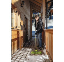 Un homme balaie la neige avec un balai devant une maison en bois